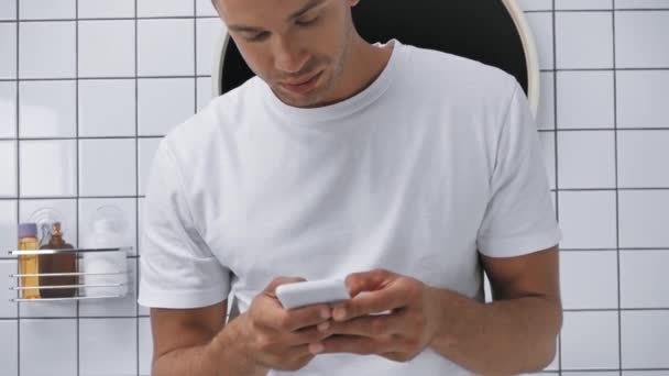 χαρούμενος άνθρωπος γραπτών μηνυμάτων στο smartphone στο μπάνιο  - Πλάνα, βίντεο