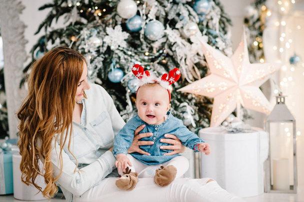 Baby girl with mom on floor near Christmas tree. Happy New Year and Merry Christmas. Christmas decorated interior. The concept of family holiday. - Fotó, kép