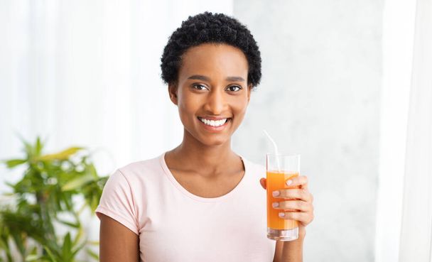 Zdrowe odżywianie i odtruwanie. Uśmiechnięta czarna kobieta ze szklanką świeżego soku pomarańczowego w domu, panorama - Zdjęcie, obraz