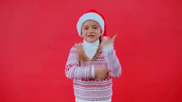 κορίτσι με το καπέλο Σάντα και το χριστουγεννιάτικο πουλόβερ χορό απομονωμένο στο κόκκινο - Πλάνα, βίντεο