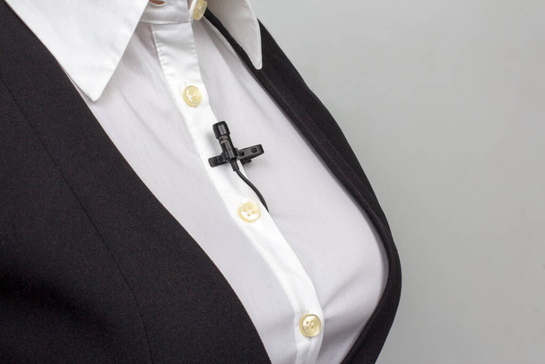 small lavalier microphone clamped to a woman's white shirt. Audio recording of the sound of the voice on a condenser microphone. - Foto, afbeelding