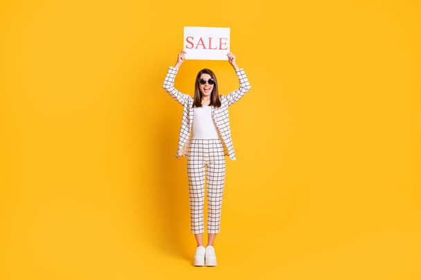 Full length body size photo of funny girl keeping sale sign wearing sunglass smiling isolated on bright color background - Foto, Imagem