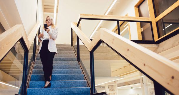Full body elegant lady in formal wear standing on steps and browsing smartphone while working in modern workspace in Barcelona City - Foto, immagini