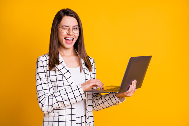 Photo portrait of pretty woman keeping laptop wearing spectacles smiling winking blinking isolated on vibrant yellow color background - Foto, immagini