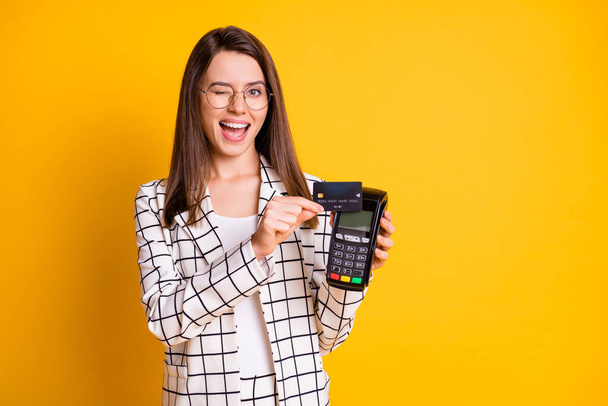 Photo portrait of young female worker doing cashless payment card terminal winking blinking isolated on vivid yellow color background - Foto, Imagen