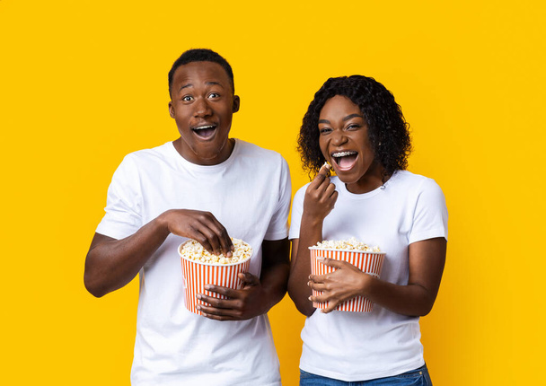 Śmiejący się czarny mężczyzna i kobieta jedzący popcorn na żółtym tle - Zdjęcie, obraz