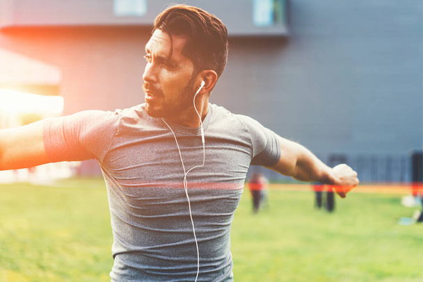Muscular male athlete warming up and exercising during outdoors endurance workout, handsome Caucasian sportsman in modern earphones listening music while having training for keep fit body shape - Foto, imagen
