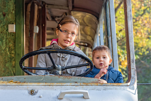 As crianças brincam num autocarro abandonado. Uma rapariga conduz um autocarro. A menina vira o volante no ônibus abandonado.  - Foto, Imagem