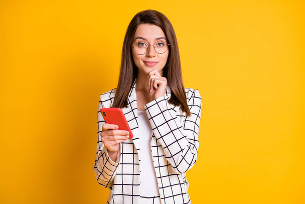 Photo portrait of clever businesswoman keeping cellphone touching face wearing checkered suit isolated on vivid yellow color background - Photo, image