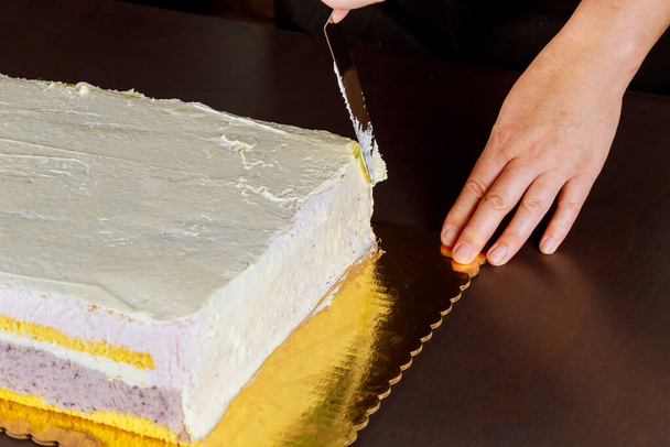 Pokrywa szefa kuchni z białym lukrem świąteczny tort. Tworzenie warstwy biszkoptu. - Zdjęcie, obraz