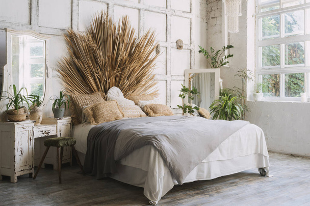 Konforlu yatak odasının yan görünüşü, iç dekorasyonu bohem tarzı, rahat yatak, yeşil ev bitkileri, tuvalet ve aynaya yakın dekorasyon. Gün ışığı ve aydınlık bir sabah - Fotoğraf, Görsel