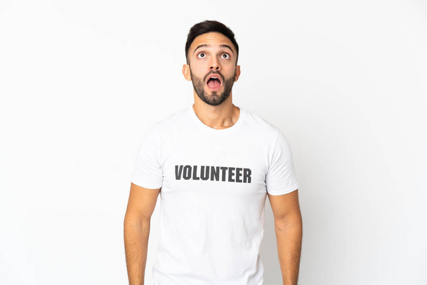 Νεαρός Καυκάσιος εθελοντής απομονωμένος σε λευκό φόντο κοιτάζοντας ψηλά και με έκπληκτη έκφραση - Φωτογραφία, εικόνα