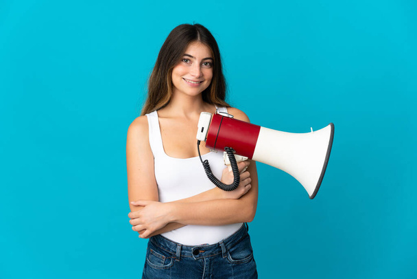 Young caucasian woman isolated on blue background holding a megaphone and smiling - Photo, Image