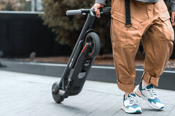 Close up of Active Man Carrying Electric Kick Scooter Near Business Center. Comfortable Transportation. Eco Transport At Cityscape. - Foto, Imagen