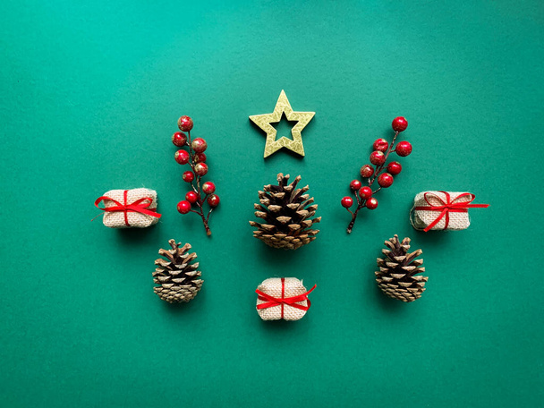 Composizione natalizia e invernale fatta di decorazioni natalizie a stella, scatole regalo, pigne e rami di bacche rosse su sfondo verde.  - Foto, immagini