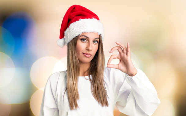 Lány karácsonyi kalap mutatja egy ok jel ujjaival át nem fókuszált háttér - Fotó, kép