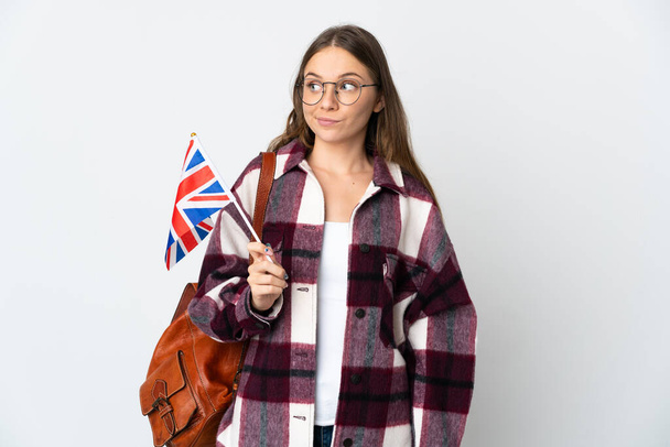 Young Lithuanian woman holding an United Kingdom flag isolated on white background making doubts gesture looking side - Photo, Image
