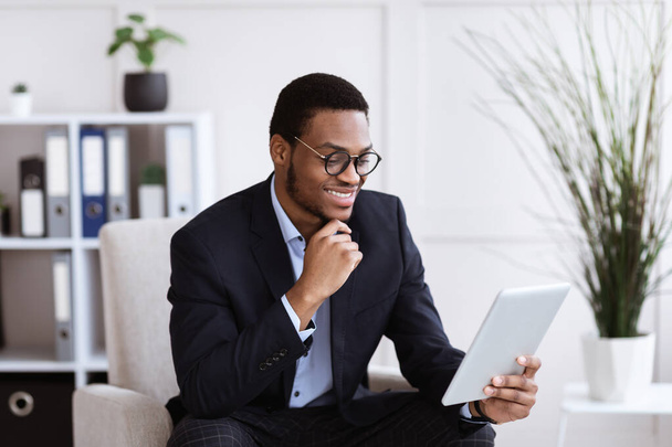 Cheerful black businessman holding digital tablet, office interior - Photo, Image
