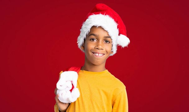 menino afro-americano com chapéu de Natal sobre fundo vermelho - Foto, Imagem