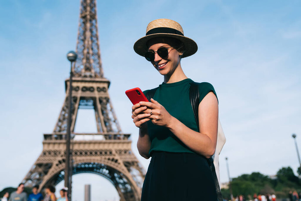 Caucasian woman browsing wireless network during time for romantic French walk in Paris, carefree female tourist enjoying smartphone communication standing at street with Eiffel Tower on background - Fotó, kép