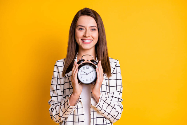 Photo of toothy beaming lady woman wear checkered outfit holding alarm in two hands isolated yellow color background - Foto, immagini