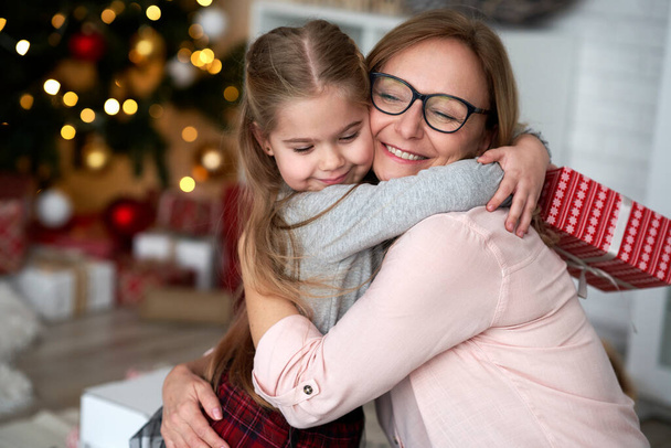 Enkelin umarmt ihre Großmutter in der Weihnachtszeit.                                - Foto, Bild