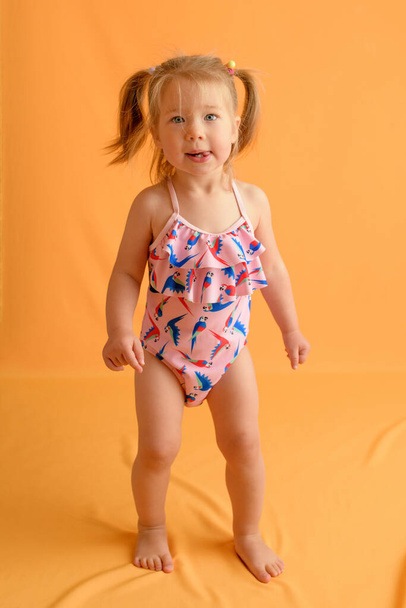 A girl at the age of one and a half years in a swimsuit. Studio photo session. Photographed with a yellow background. - Photo, Image