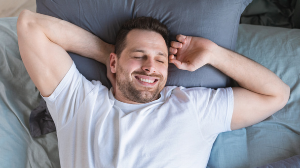 Guy probouzející se natažené ruce ležící v posteli, pohled shora - Fotografie, Obrázek