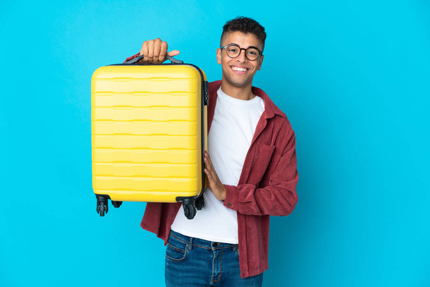 Young Brazilian man over isolated background in vacation with travel suitcase - Photo, Image