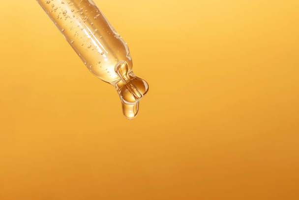 macro van pipet met vloeistof en druppel op gouden achtergrond - Foto, afbeelding