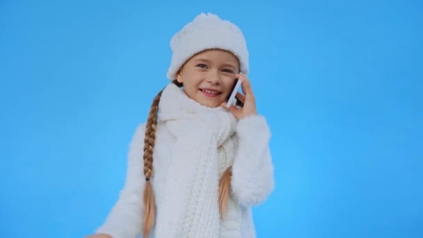 girl in knitted white winter outfit talking on smartphone isolated on blue - Footage, Video