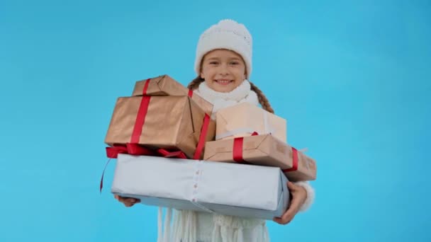 девушка в трикотажном белом зимнем наряде бросает подарочные коробки изолированы на синий - Кадры, видео