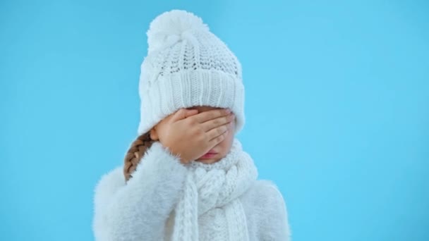 προσβεβλημένη κοπέλα με πλεκτό λευκό χειμωνιάτικο ντύσιμο κλαίει απομονωμένη στο μπλε - Πλάνα, βίντεο