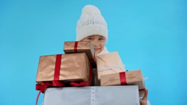 девушка в трикотажном белом зимнем наряде с подарочными коробками изолированы на синий - Кадры, видео