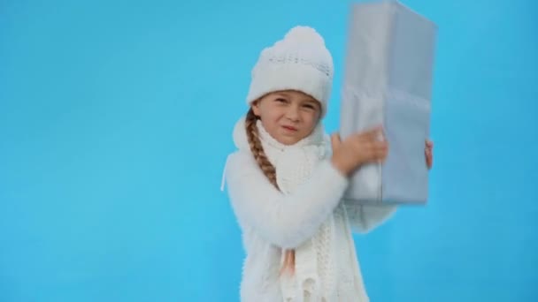 Девушка в трикотажном белом зимнем наряде трясущаяся подарочная коробка изолирована на синий - Кадры, видео