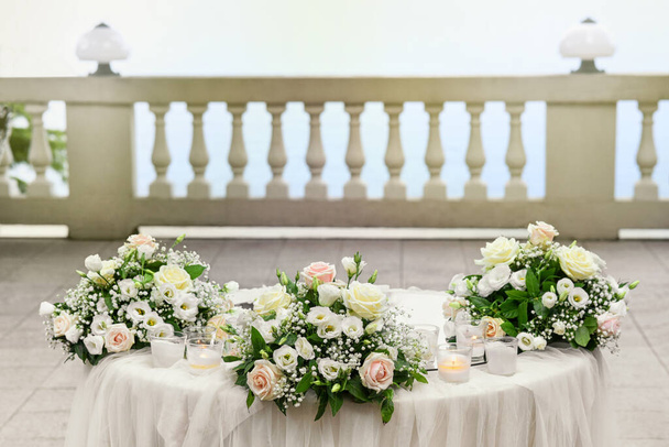 Açık hava verandasında üç demet pembe ve beyaz çiçek ve mumla süslenmiş şık bir açık hava düğün masası. - Fotoğraf, Görsel