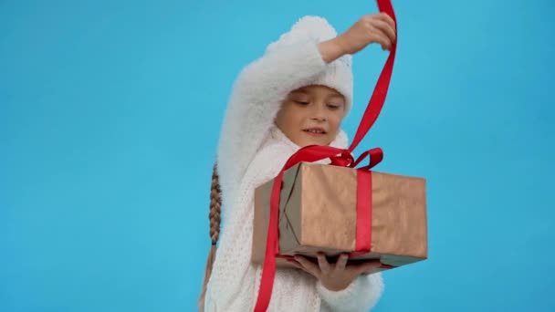 meisje in gebreide witte winter outfit opening geschenk doos geïsoleerd op blauw - Video
