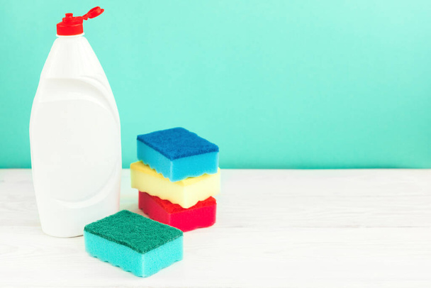 Bottle of dish washing, sponges, utensils on white wooden table against a green wall background - Φωτογραφία, εικόνα