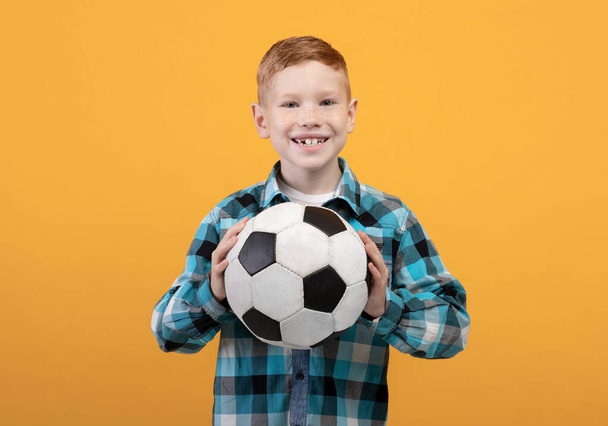 Boy posing with soccer ball on yellow studio background - Foto, afbeelding