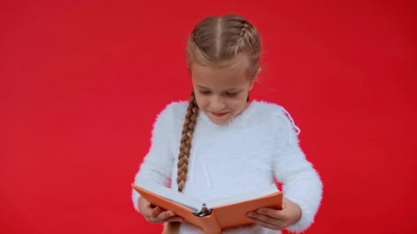 Mädchen im flauschigen Pullover liest Buch isoliert auf rot - Filmmaterial, Video