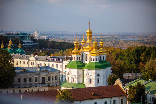 Gyönyörű sárga és arany kupolák az ortodox egyház hátterében a kék ég és a város. Domes of the Assumption Cathedral of the Kiev-Pechersk Lavra. - Fotó, kép