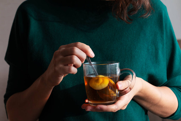 femme en pull vert tient une tasse de thé au citron chaud - Photo, image