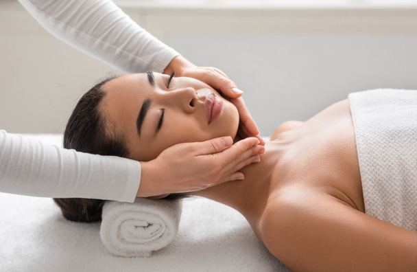 Tratamiento de belleza facial. Mujer asiática recibiendo masaje lifting facial en el gabinete de cosmetología - Foto, imagen