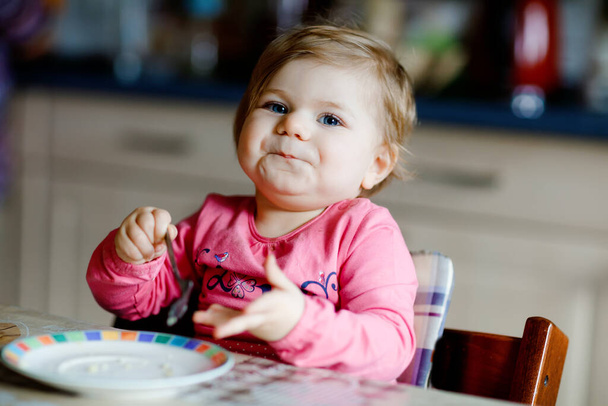 Šťastná holčička jí čerstvý croissant k snídani nebo obědu. Zdravé stravování pro děti. batole dítě v barevném pyžamu sedí v domácí kuchyni po spánku v dopoledních hodinách - Fotografie, Obrázek
