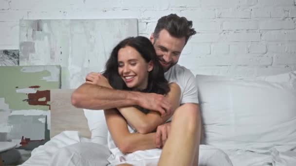 happy man tickling cheerful girlfriend in bedroom - Záběry, video