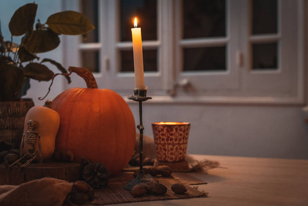 Halloween pumpkin with candle lit in a table. Skeleton, candles, nuts. Teal and orange beautiful still life. - Foto, afbeelding