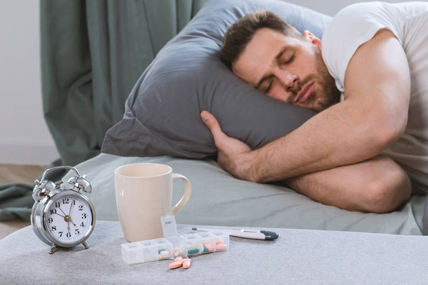 Άνδρας που ξεκουράζεται στο κρεβάτι μετά τη λήψη υπνωτικών χαπιών στο υπνοδωμάτιο - Φωτογραφία, εικόνα
