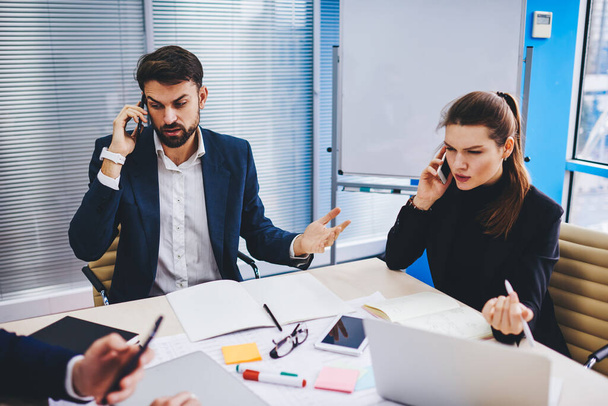 Experienced male and female bankers calling to customers for discussing mortgage deal using smartphone gadgets in office interior, Caucasian executive managers solving business problems while phoning - 写真・画像