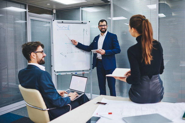 Male and female experts have coaching conversation for discuss statement for project checking infographics on flip chart, businessman communicating with office employees explaining revenue benchmark - 写真・画像