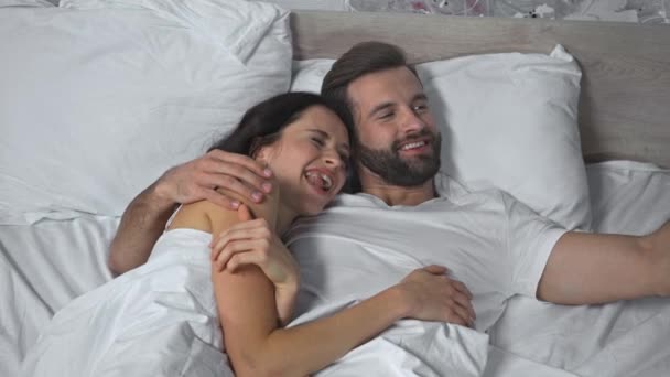 alegre pareja acostada en la cama y tomando selfie  - Imágenes, Vídeo